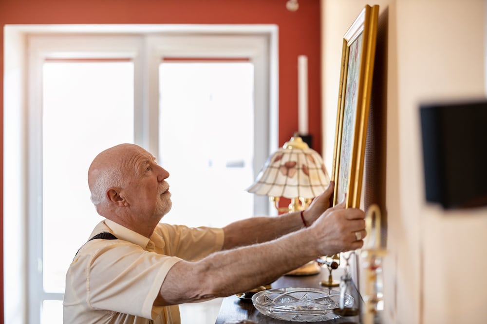 A senior man raccrochant un tableau dans son appartement